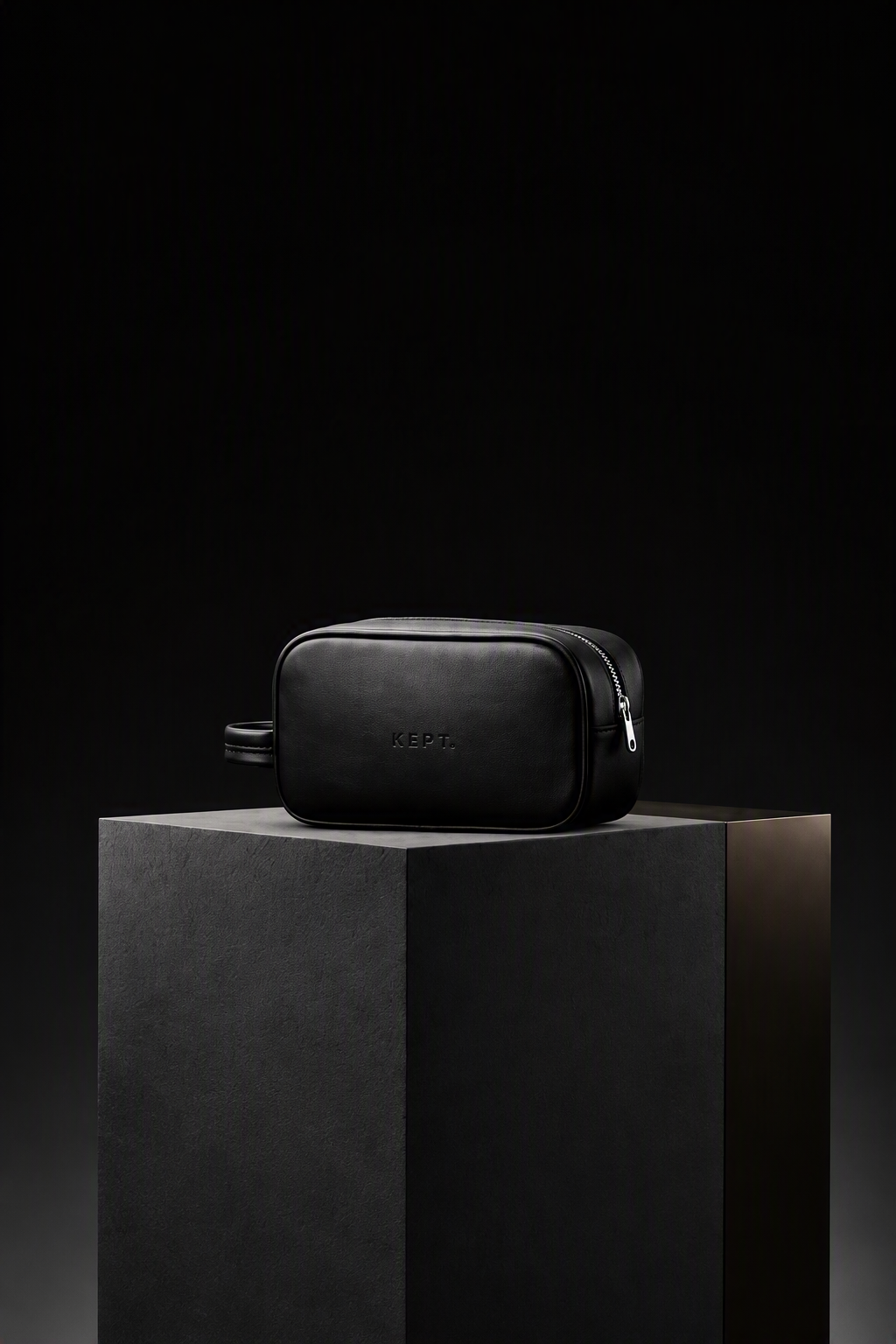 KEPT premium black leather toiletry bag displayed on a minimalist dark pedestal
