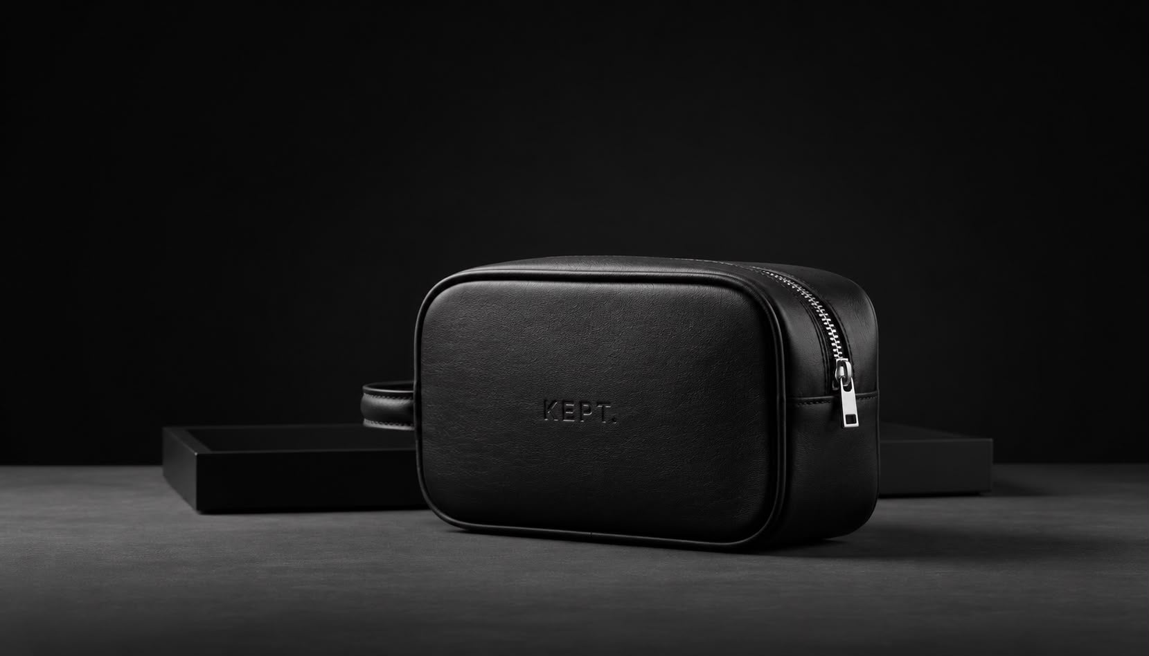 KEPT premium black leather toiletry bag with zip closure displayed against a minimalist dark background